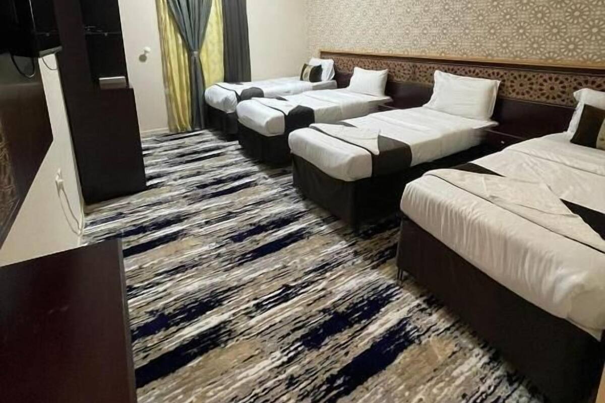 Een hotelkamer met drie bedden, een televisie en een kamerbreed tapijt met een patroon.