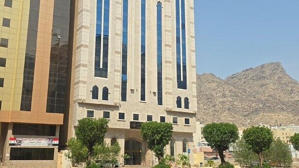 A modern building with large windows and a flat roof, surrounded by a road and trees. - Al Resala Al Masi Hotel (Makkah)
