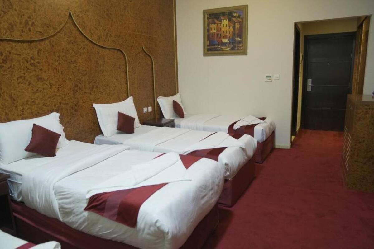 Een hotelkamer met twee eenpersoonsbedden, een houten hoofdeinde, een rood tapijt en een schilderij aan de muur.