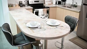 A modern kitchen with a marble countertop, two black chairs, and a dining table set for two. - Premium Suite at The Vineyards (Kingston)