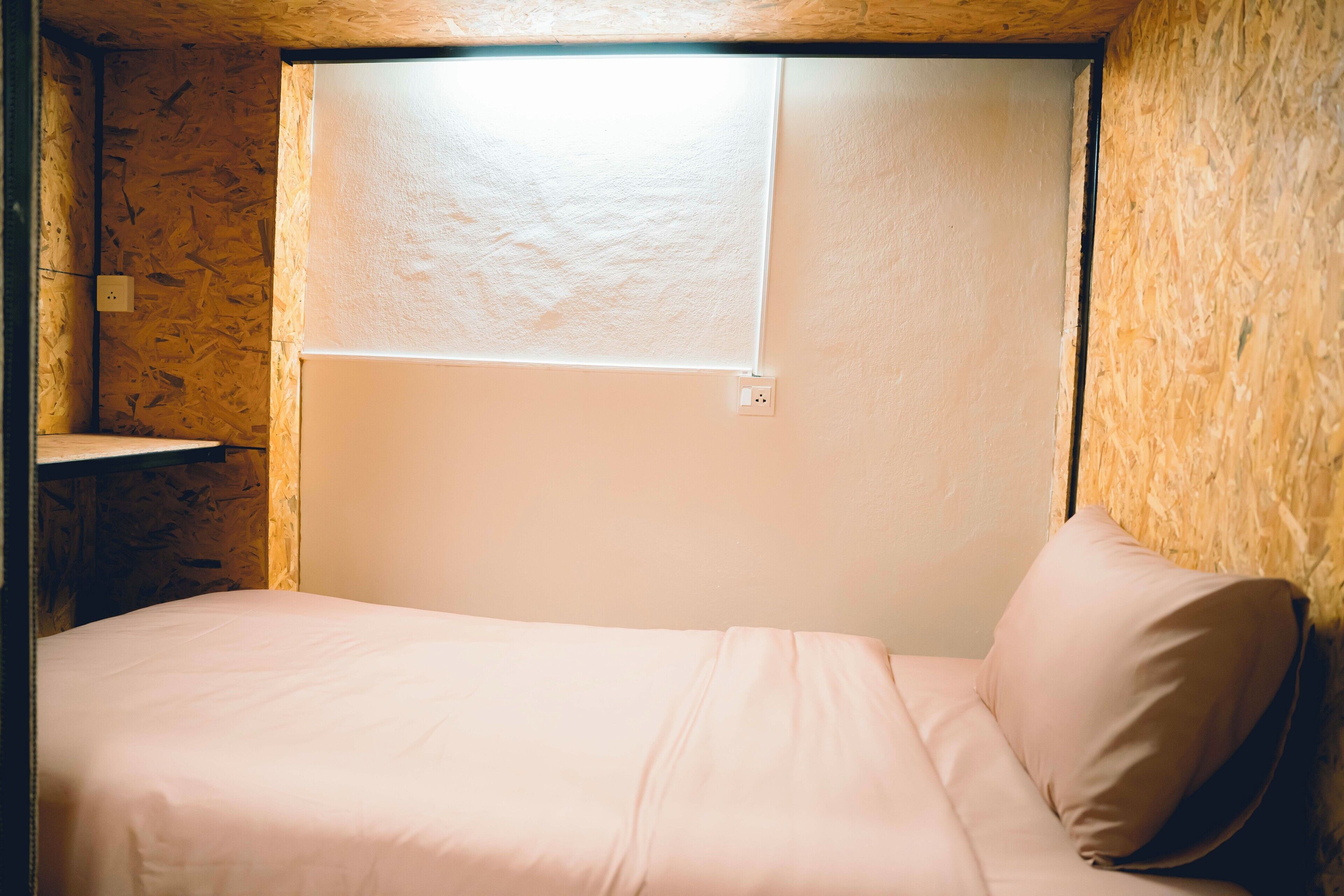 A small, cozy room with a single bed, a window, and a wooden wall.