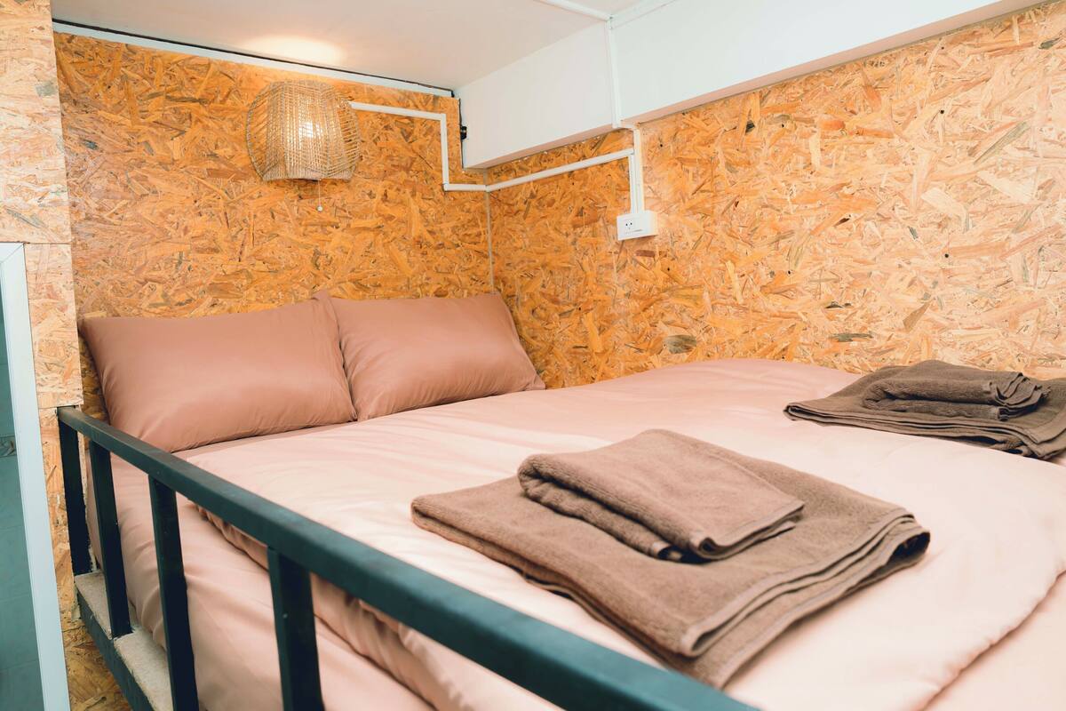 A single bed with a metal frame, pink bedding, and a folded towel on top.