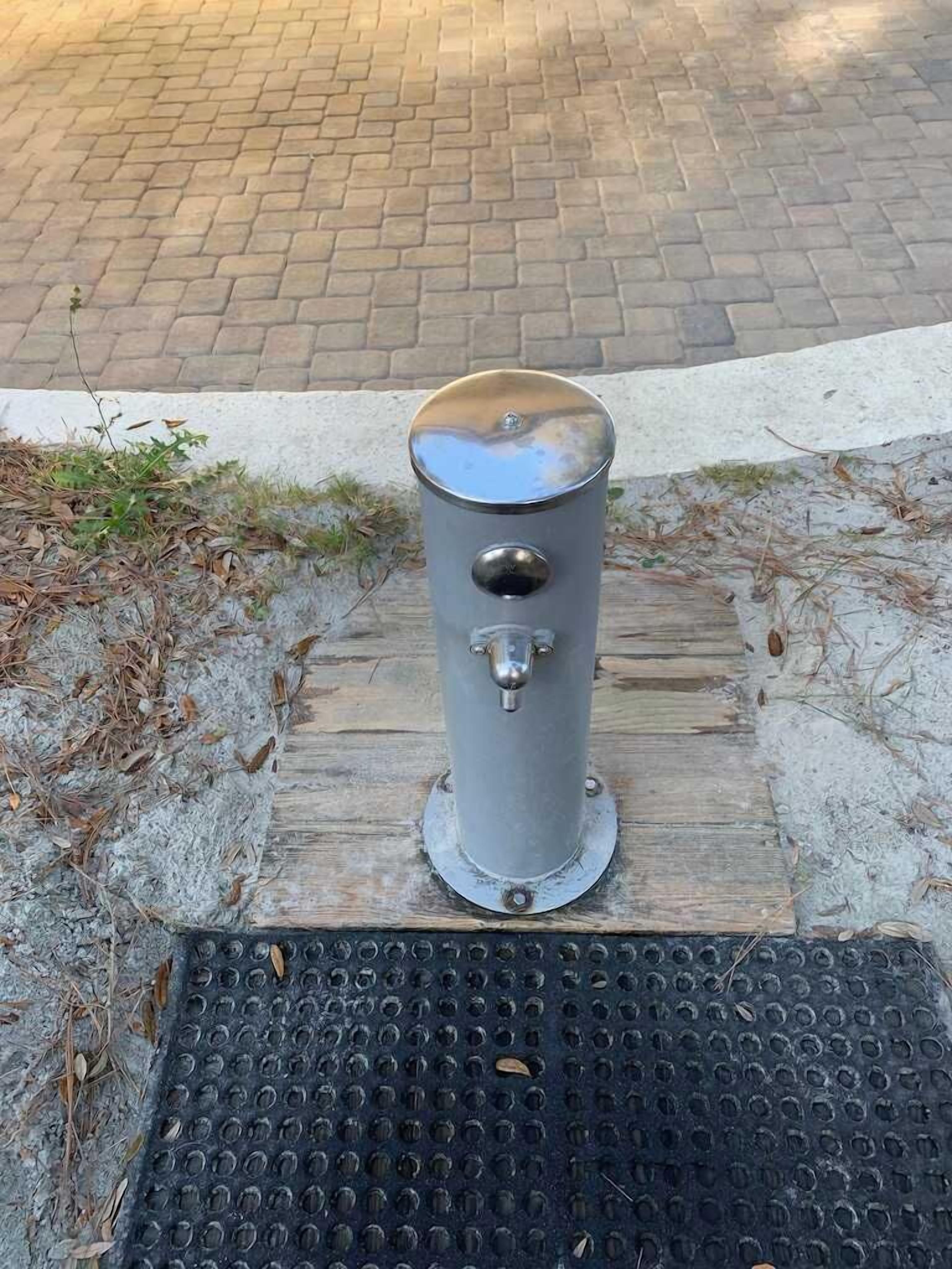 A metallic fire hydrant on a wooden plank with a metal grate below.