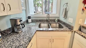 Una cocina con encimera de granito, pileta de acero inoxidable y cafetera.