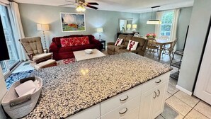 Amplia sala de estar con una isla grande, un sofá rojo, un sillón color beige y una mesa de comedor con sillas.