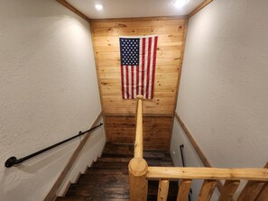 A wooden staircase with a handrail, a wooden wall, and an American flag hanging on the wall.
