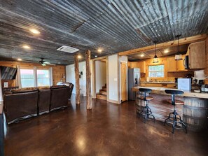 A spacious kitchen with a wooden bar area, a refrigerator, and a large window.