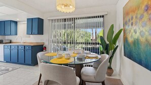 A modern kitchen with blue cabinets, a dining area with a glass table, yellow placemats, and a large abstract painting on the wall.