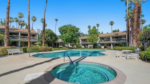 A hotel pool area with two circular pools, palm trees, and lounge chairs.