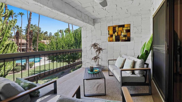 A balcony with a view of a pool, a sofa, a coffee table, and a decorative plant.