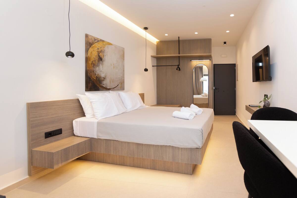 Quarto de hotel moderno com cama, mesa de cabeceira e televisão na parede.