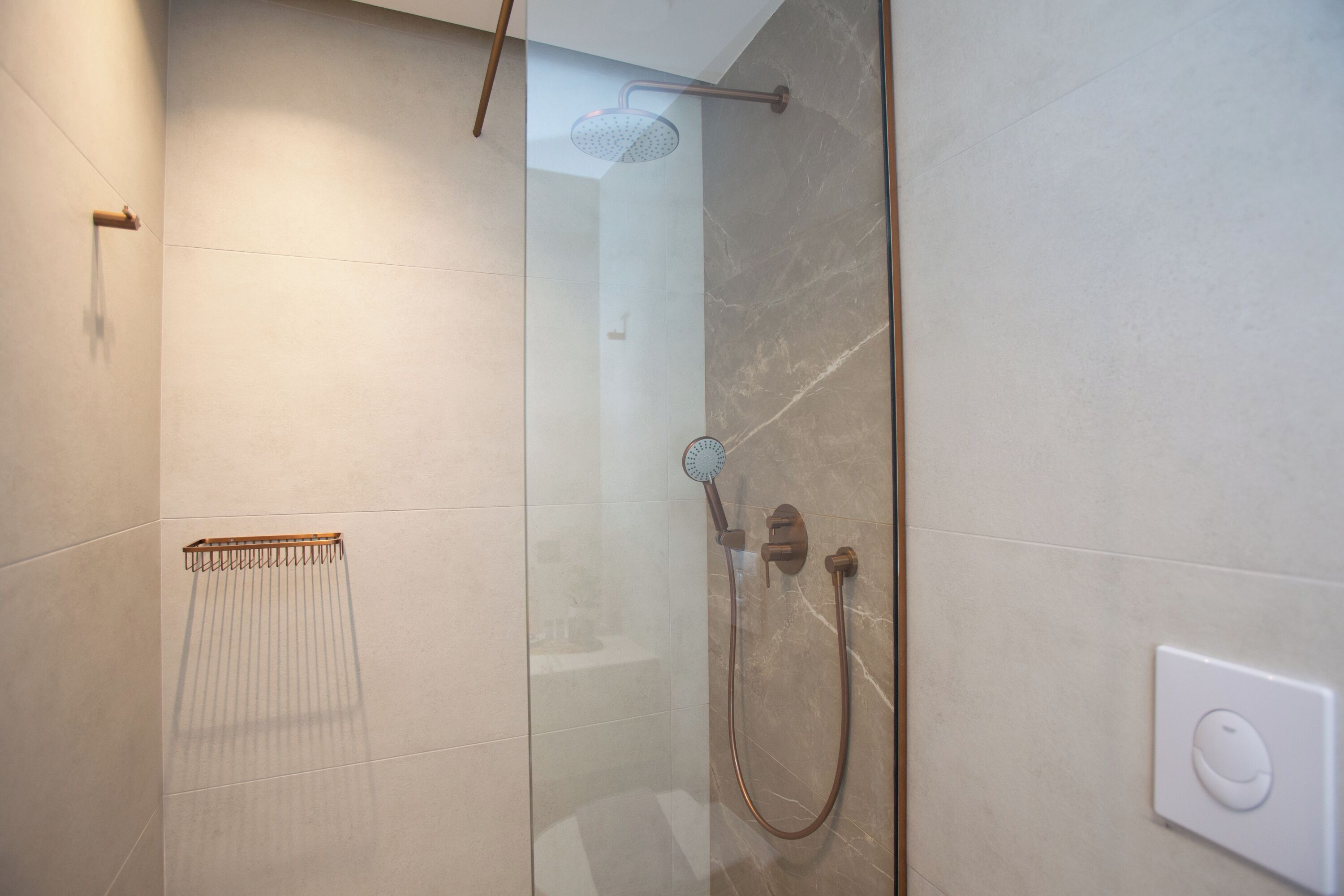 Une douche moderne dotée d’une porte en verre, d’un pommeau de douche à main et de commandes murales.