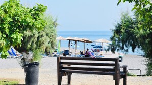 Une plage avec un banc en bois, des parasols et des chaises longues.