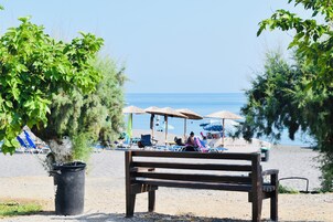 Una playa con un banco de madera, sombrillas y sillas de descanso.