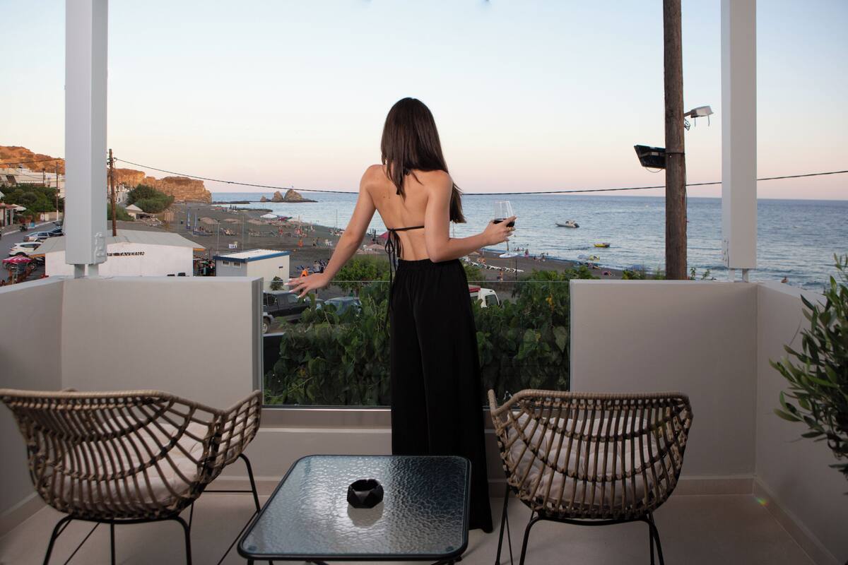 Uma varanda com vista para o mar, cadeiras de vime e uma mesa.