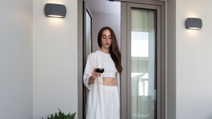 Une personne se tient devant une porte-fenêtre coulissante et tient un smartphone.