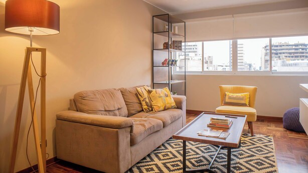 A modern living room with a sofa, a coffee table, a floor lamp, and a bookshelf. - Sophisticated 1BR Stay in Prime Miraflores (Lima)