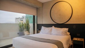 A modern bedroom with a large bed, a circular wall decoration, a small bedside table, and a view of the city through a large window. - w Scenic 1BR w Terrace in Barranco (Lima)