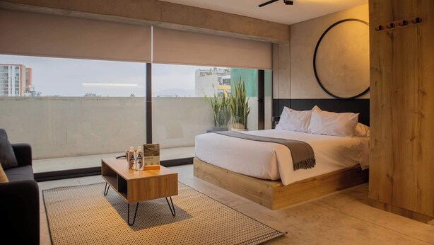 A modern bedroom with a large bed, a wooden bedside table, a small coffee table, and a view of the city through large windows. - w Scenic 1BR w Terrace in Barranco (Lima)