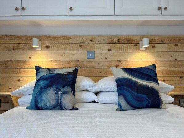 Une chambre à coucher avec une tête de lit en bois, une literie blanche et deux coussins décoratifs aux motifs abstraits.
