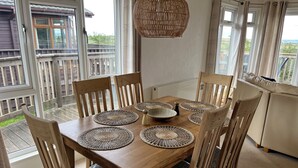 Uma mesa de jantar de madeira com jogos americanos trançados, seis cadeiras e um lustre pendurado.