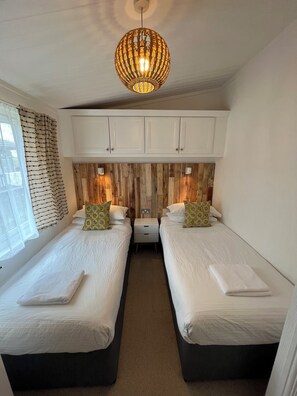 Une chambre avec deux lits, un panneau mural en bois, un plafond blanc et un luminaire suspendu.