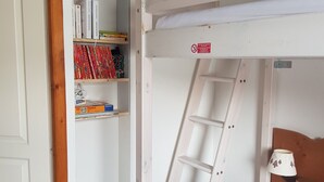 Un lit superposé avec une échelle, une bibliothèque remplie de livres et de jeux de puzzle, et une table de chevet avec une lampe.