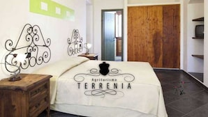 A bedroom with a bed, a wooden nightstand, a wall-mounted decorative metal piece, and a door. - Laboratorio Gourmet (Taormina)