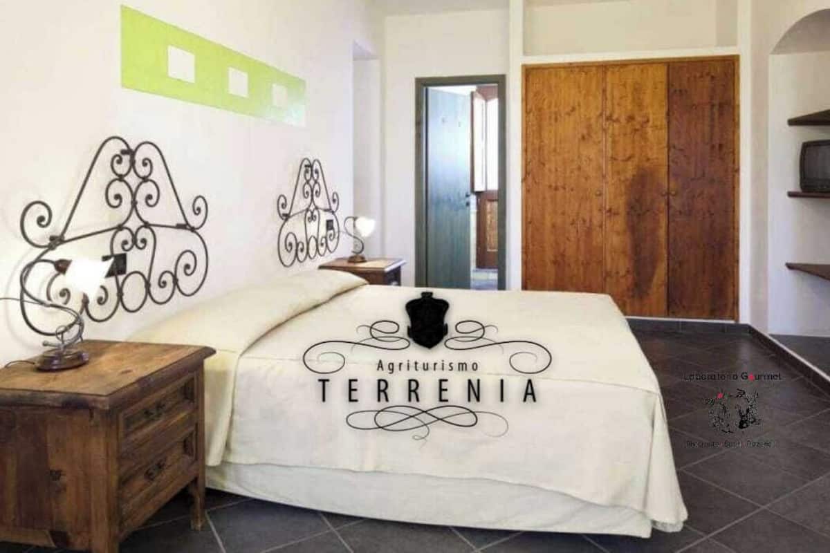 A bedroom with a bed, a wooden nightstand, a wall-mounted decorative metal piece, and a door.