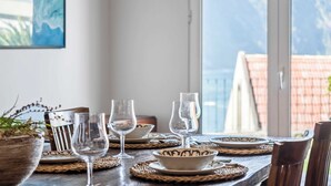 Ein Esstisch ist mit Tellern, Schüsseln und Weingläsern gedeckt, mit Blick auf Berge durch ein Fenster.