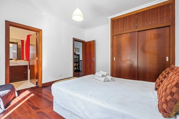 Quarto com cama grande, guarda-roupa de madeira e banheiro com cortina de chuveiro vermelha.