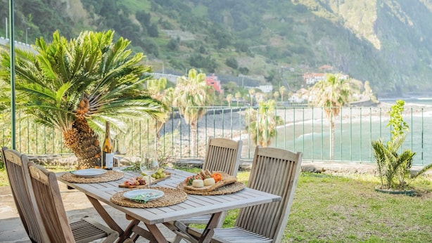 Ein Essbereich im Freien mit einem Tisch für vier Personen, mit Blick auf eine K üstenlandschaft und Meer sowie Hügel.