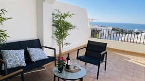 Un balcon avec un canapé, des chaises, une table sur laquelle se trouvent une bouteille, des verres et une plante.