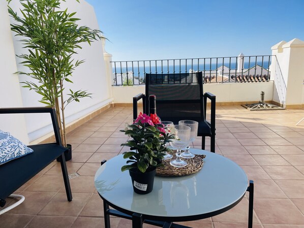 Ein runder Glastisch mit einem Blumentopf und Gläsern auf einem Balkon mit Meerblick.