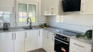 Une cuisine moderne avec des meubles blancs, une hotte noire, un four encastré et une fenêtre avec des stores.