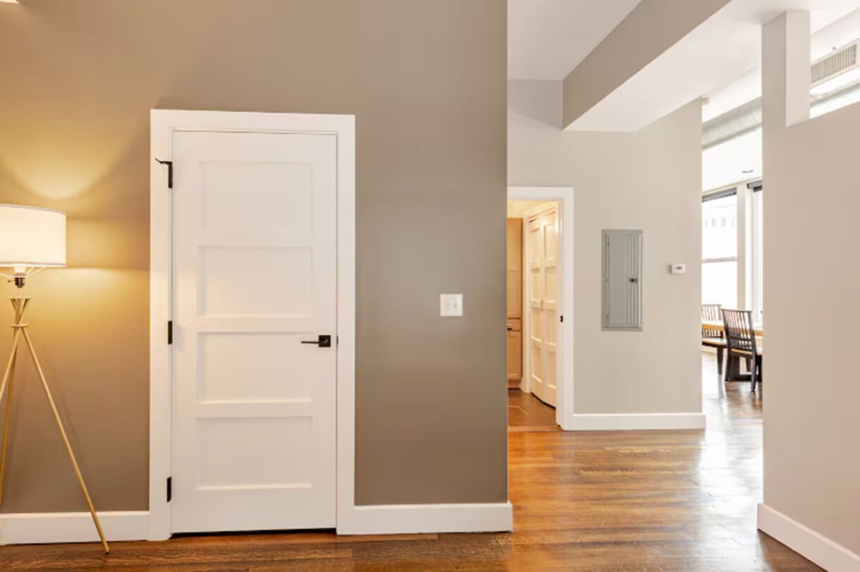 A hallway with a white door, a lamp, and a bench in the distance.