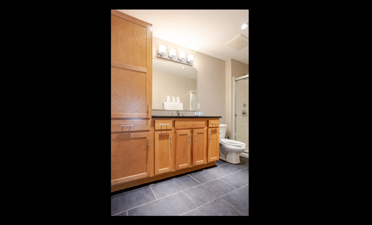 A bathroom with wooden cabinets, a black countertop, and a white toilet.