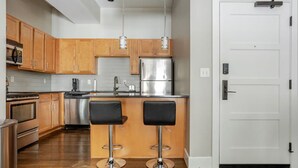 Een moderne keuken met houten kastjes, roestvrijstalen apparatuur en twee barkrukken.