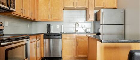 A modern kitchen with wooden cabinets, stainless steel appliances, and a black countertop.