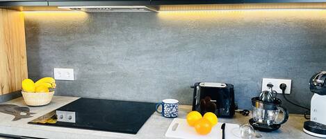A modern kitchen with a black induction cooktop, a Philips toaster, a coffee maker, and a basket of fruit.
