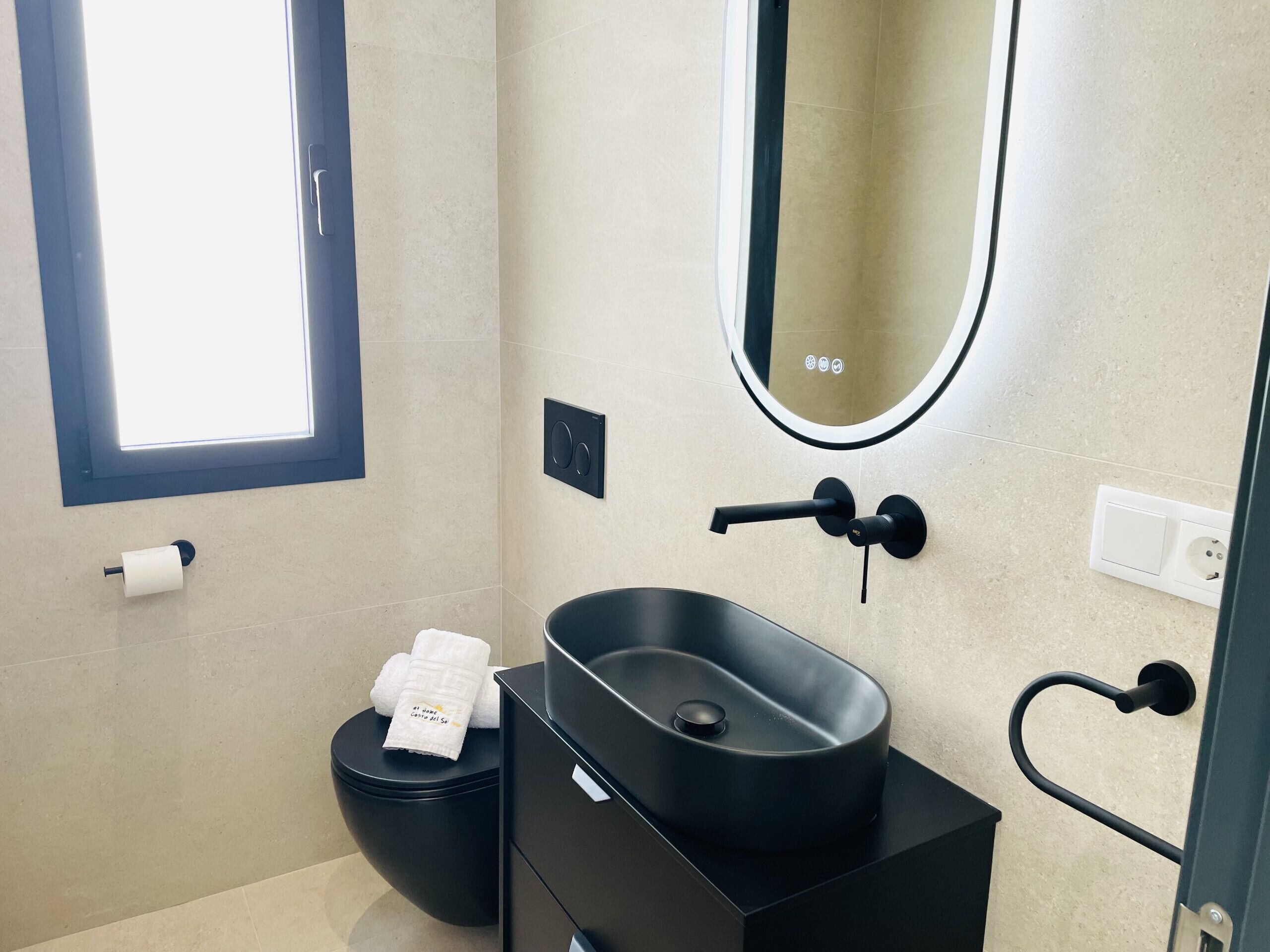Ein modernes Badezimmer mit schwarzem Waschbecken, WC und Waschtisch.