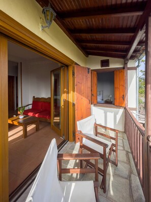 A covered outdoor area with a red sofa, wooden chairs, and a table. - Stay Horizon P1 Milies (South Pelion)