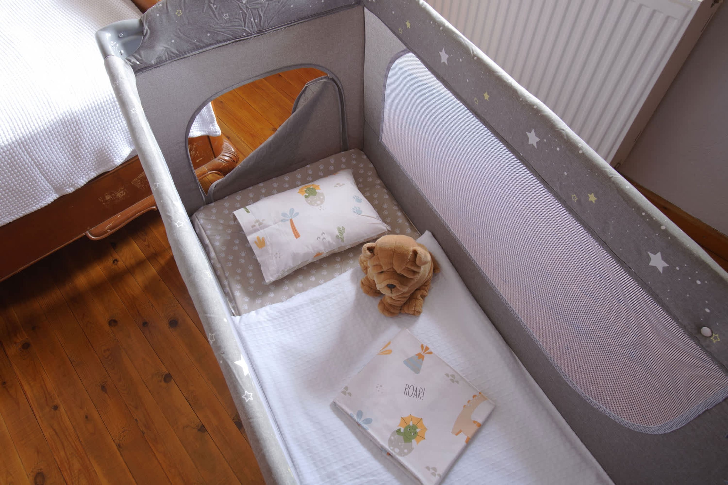 A baby crib with a grey frame, white mattress, and a teddy bear on the mattress.