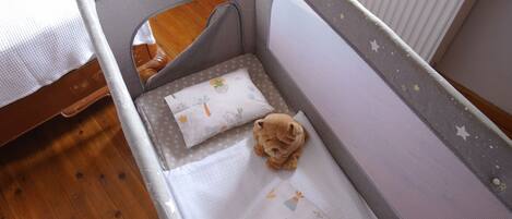 A baby crib with a grey frame, white mattress, and a teddy bear on the mattress.