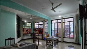 Un espace repas avec des tables et des chaises, de grandes fenêtres avec des barreaux en métal et un ventilateur de plafond.