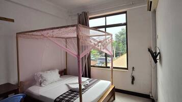 A single bed with a canopy, a ceiling fan, a window with a view of the outside, and a blue chair.