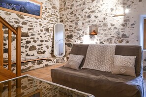 Une pièce avec un mur en pierre, un lit recouvert d’une literie à motifs, un escalier en bois et un tableau encadré accroché au mur.
