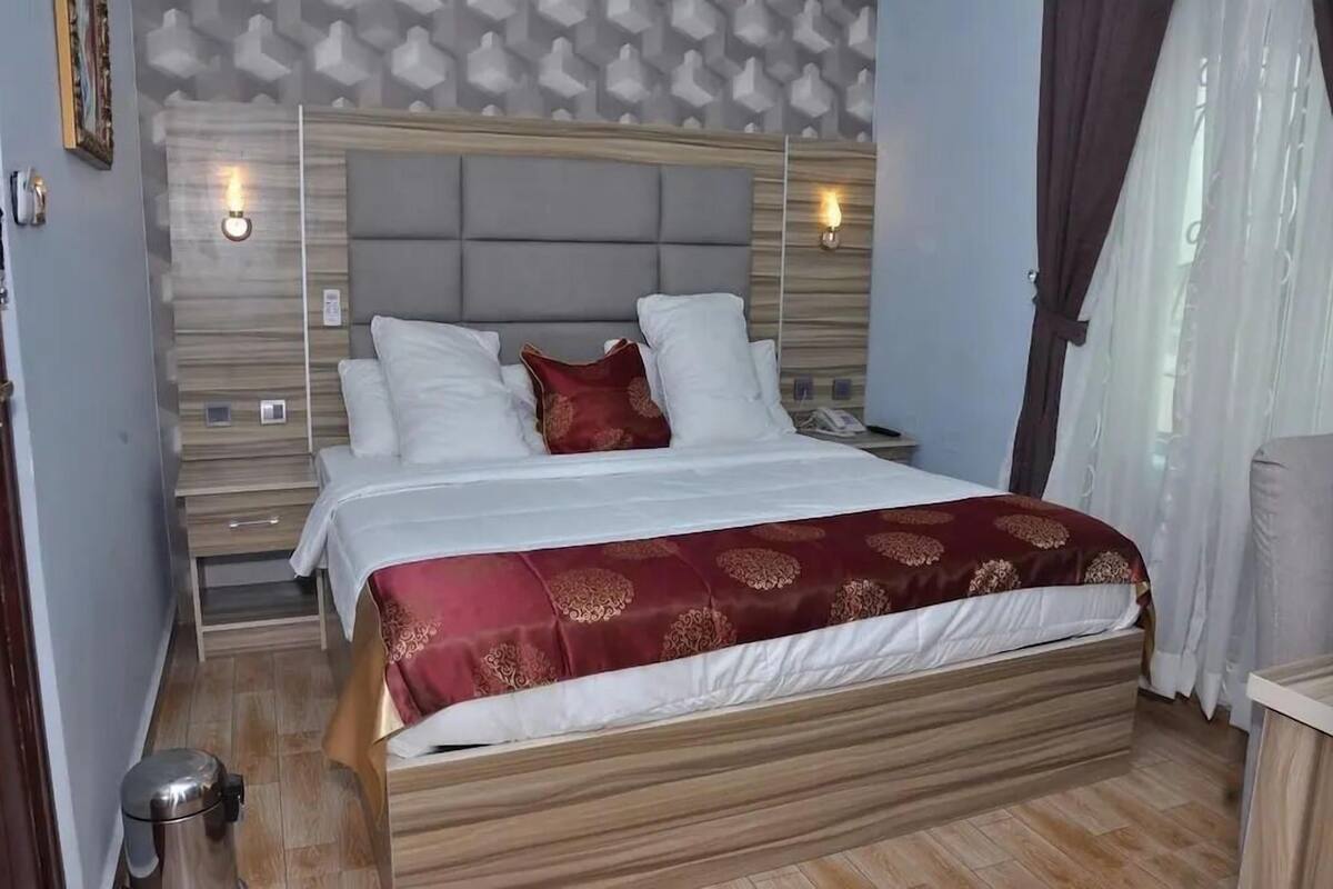 Ein Hotelzimmer mit Bett, Nachttischen, einem Mülleimer und einer Wandleuchte.