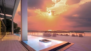 Un espace piscine aménagé sur le toit, offrant une vue sur le coucher de soleil sur l’océan, avec une terrasse en bois et des chaises longues.