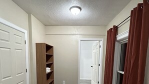 A hallway with a wooden bookshelf, white doors, and a window with red curtains.